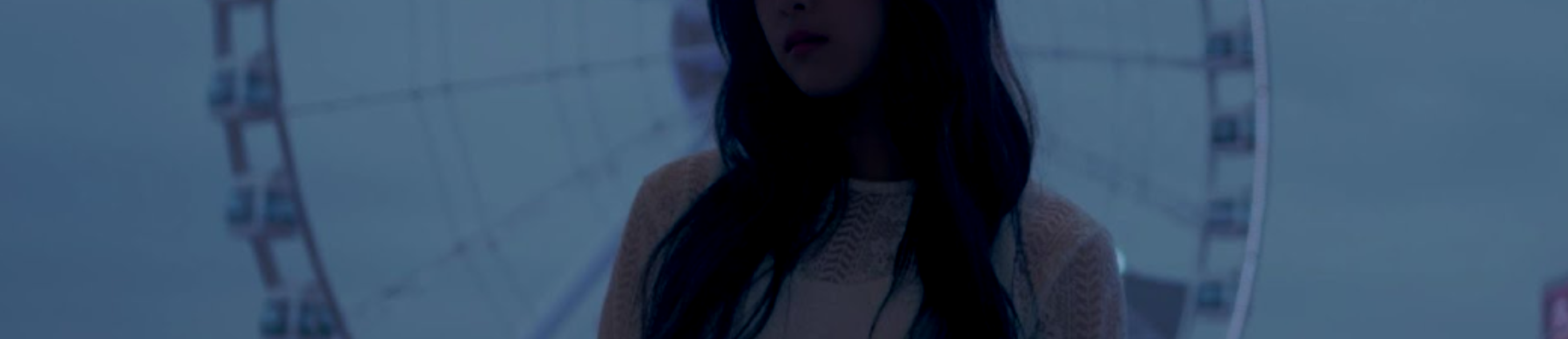 A cropped screenshot of the Sonatine music video. Hyunjin stands in the middle, wearing a white dress. She has long black hair and is almost a silhouette. Behind her is a large ferris wheel, with a cloudy blue-gray sky in the background.