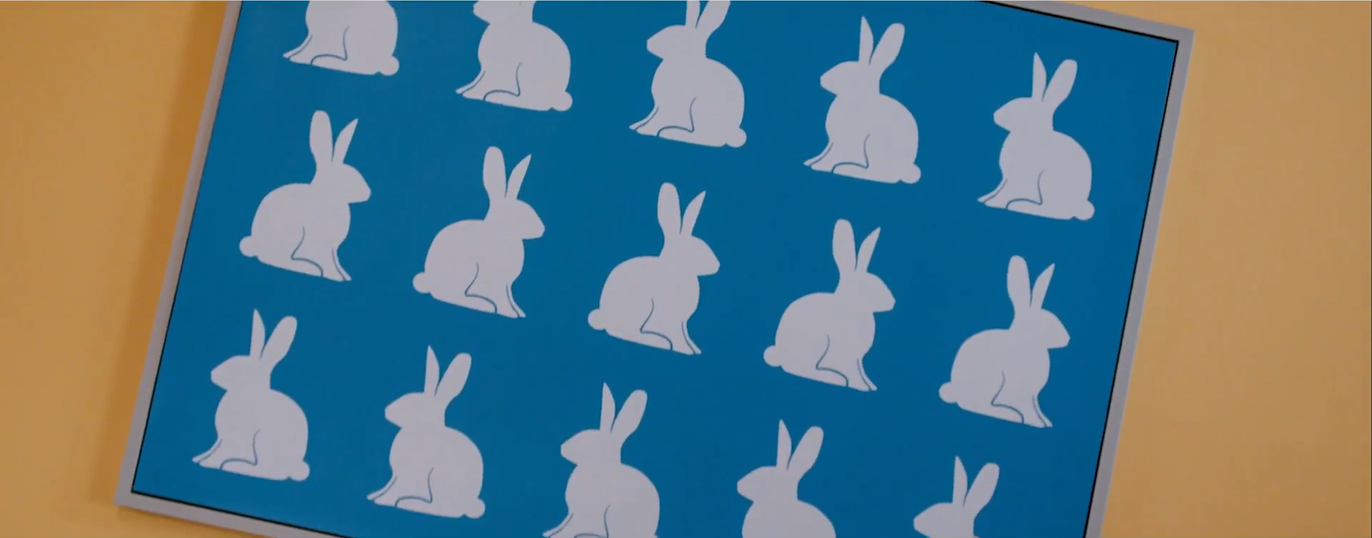 A screenshot of a painting hanging on a yellow wall. The background of the painting is blue, with fifteen white rabbits drawn over it.