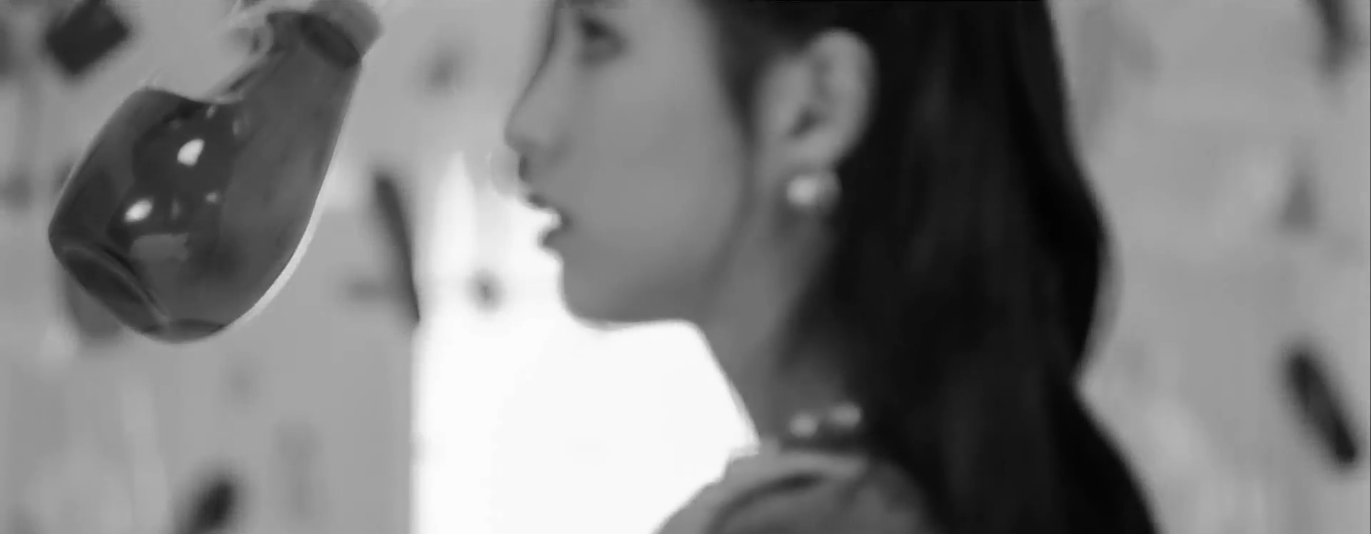 A screenshot of Heejin in the bathroom. She is looking around in awe like before, only now the entire image is in black and white.