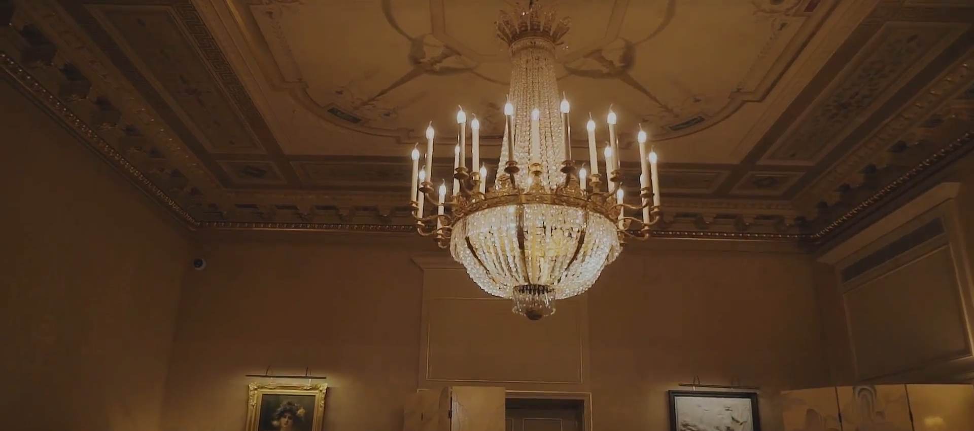 A screenshot of a lavish golden chandelier hanging from the ceiling of an ornate golden room.