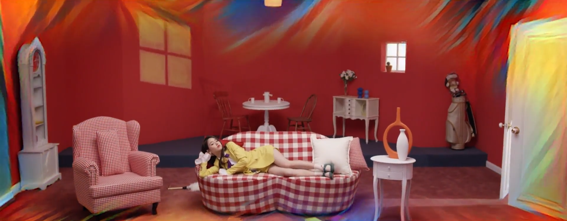 A screenshot of Heejin in the yellow outfit laying on the couch like before. The painting effect is fading away.