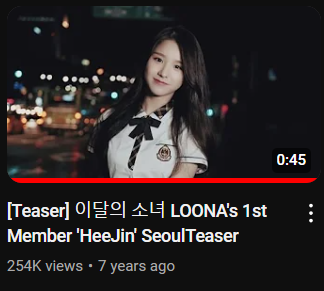 A screenshot of the thumbnail for '[Teaser] LOONA's 1st Member HeeJin Seoul Teaser.' The thumbnail is Heejin smiling at the camera, wearing a schoolgirl outfit with a blurry nighttime cityscape behind her. Text on screen shows that the video has 254k views, was posted 7 years ago, and is 45 seconds long.