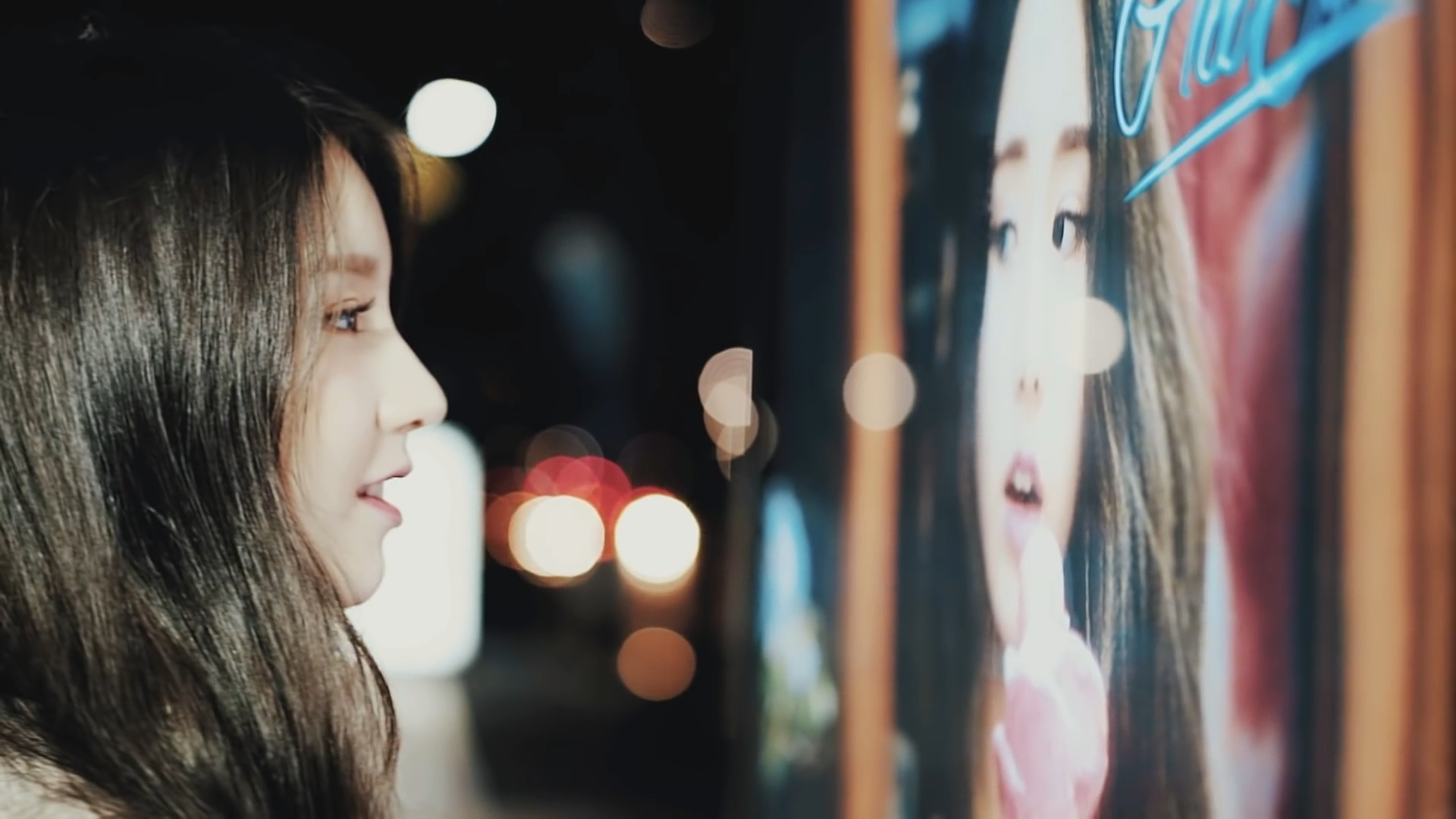 A screenshot from '[Teaser] LOONA's 1st Member HeeJin Seoul Teaser.' Heejin is staring at a picture of herself, with a smile.