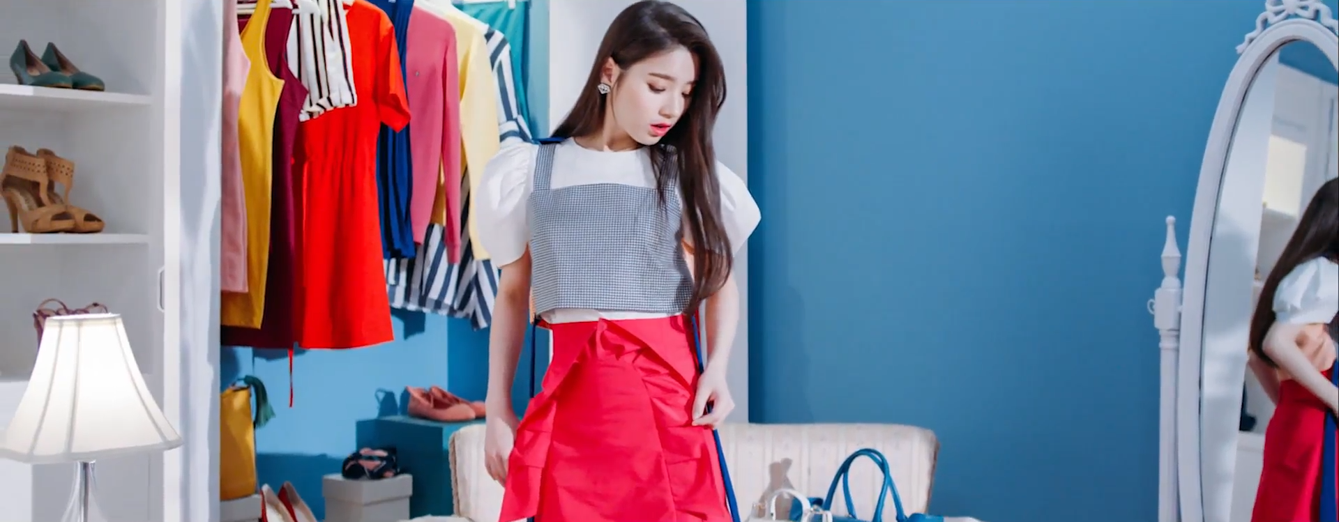 A screenshot of Heejin. She is still in the same spot as the previous images, but now she's wearing the dress she was holding. She is looking down at herself, examining how it looks on her.