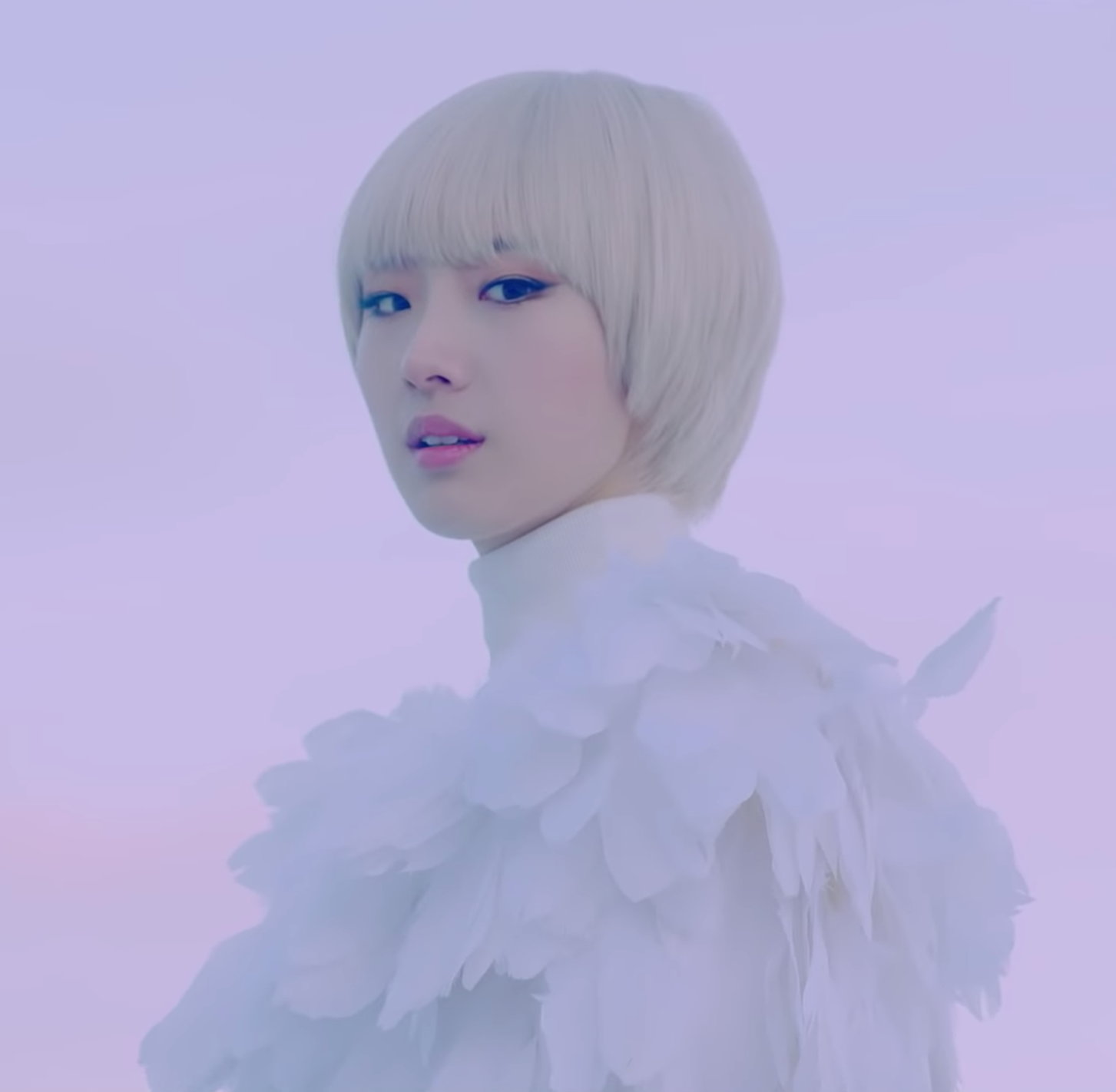 Haseul as Boyseul from the Let Me In music video. They have short blonde, almost white, hair styled in a bowlcut. They are wearing a white top made out of feathers. Their body is faced to the left, with their head turned to look directly at the viewer. The background is a light purple-pink color.