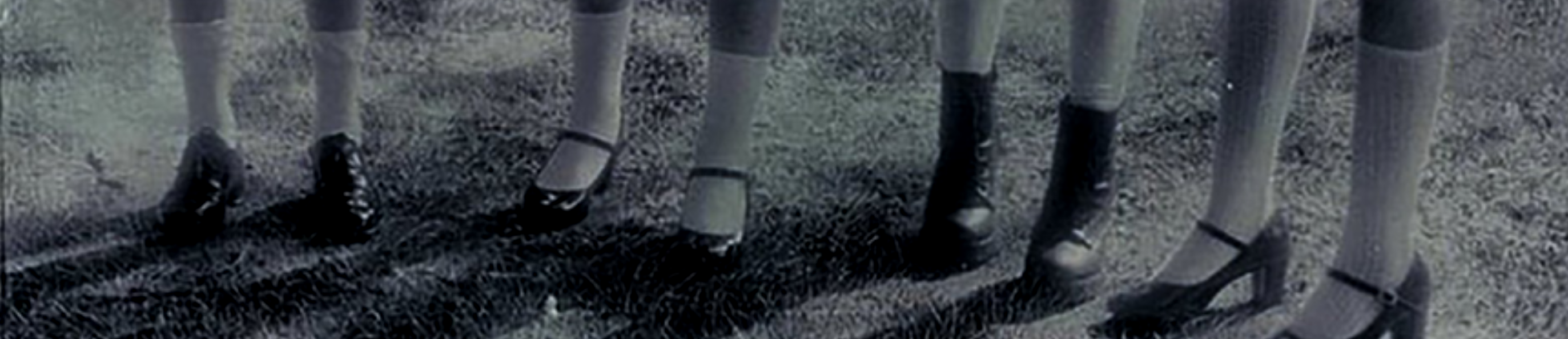 A cropped image of the members of yyxy's legs standing on grass. They are wearing black shoes with white socks. The image is in black and white.