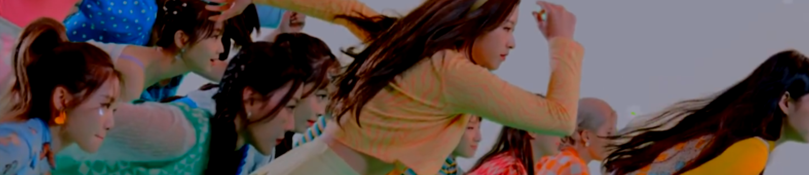 A cropped screenshot from the Hula Hoop music video. The members of Loona are all running from the left to the right, distributed across the shot. They are all wearing brightly colored clothing. The background is a white void.